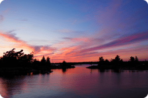 A sunset over a lake with pine trees in the background